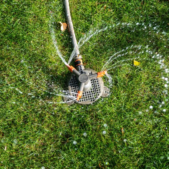 Landscape automatic garden watering system with different rotating sprinklers installed on turf. Landscape design with lawn and fruit garden irrigated with smart autonomous sprayers at sunset time.